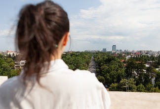 Back front of woman looking at panoramic view of metropolitan city standing on tower terrace of enjoying summer vacation. Urban skyscraper rooftop and aerial view. Landscape of buildings